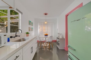 A modern kitchen with white cabinetry, a pink refrigerator, and a dining area with a white table and chairs. - Spirit of Sofia 11bd (Palm Springs)
