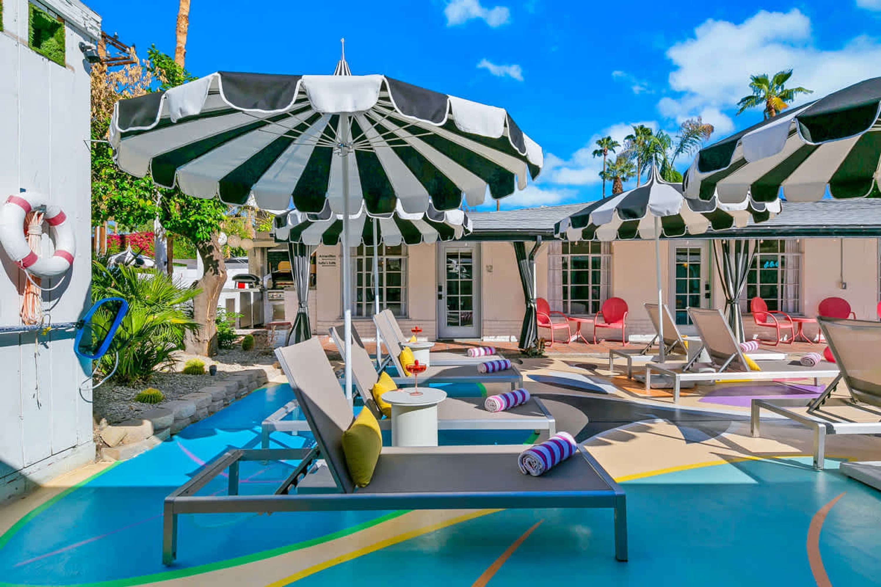 Un espace aménagé au bord de la piscine, avec des chaises longues, des parasols à rayures et une bouée de sauvetage.