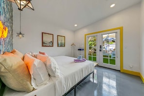 A bedroom with a bed, a door leading to an outdoor area, and a wall with framed pictures. - Spirit of Sofia 11bd (Palm Springs)