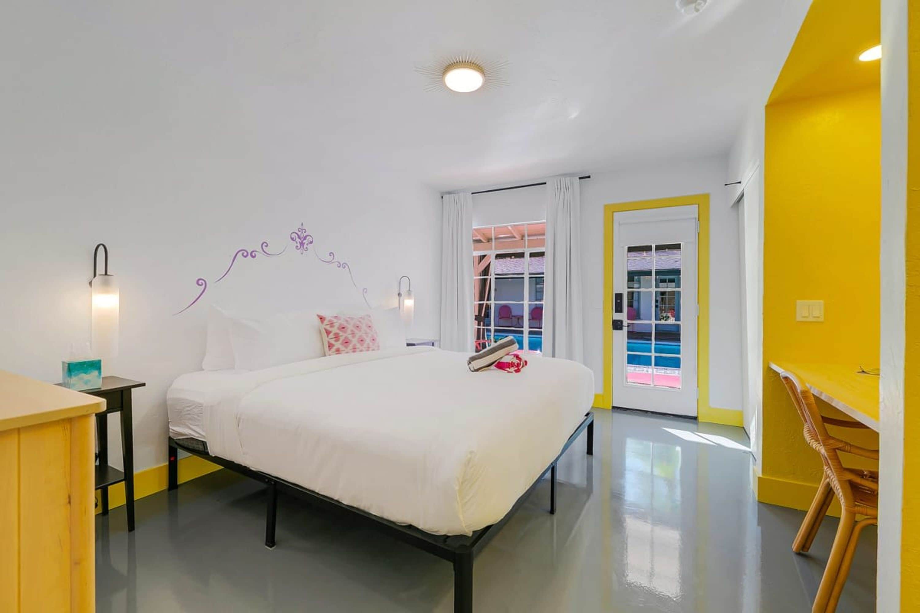 A modern bedroom with a bed, bedside tables, a desk, and a door leading to a balcony.