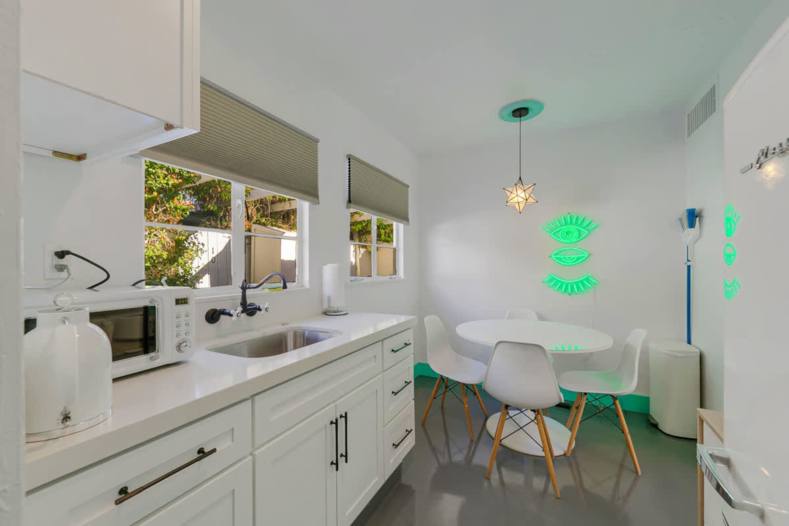 A modern kitchen with white cabinets, a microwave, a sink, and a dining area with a white table and chairs.