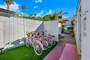 Un patio trasero con una valla blanca, una bicicleta rosa y un pequeño espacio de patio.