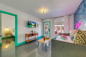 Una sala de estar moderna con un sofá, una mesita con un florero, un televisor montado en la pared y un papel tapiz estampado.