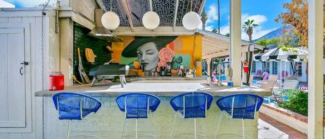 A bar area with a mural, outdoor seating, and a poolside view.