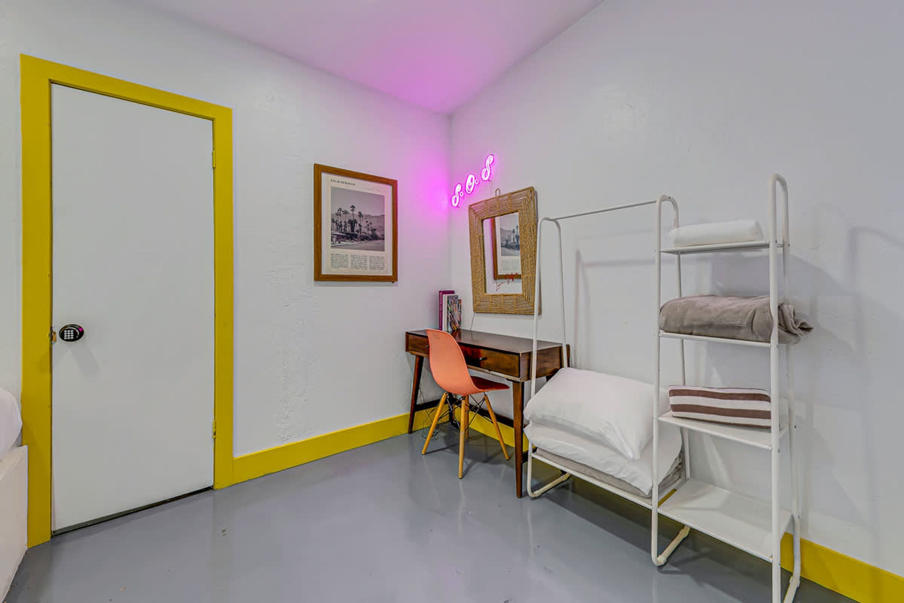 Une pièce avec un lit superposé, un bureau avec une chaise, une porte et deux tableaux encadrés au mur.