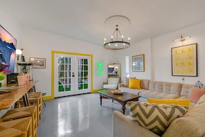 A living room with a sofa, chairs, a coffee table, a television, and a door with glass panels. - Spirit of Sofia 11bd (Palm Springs)