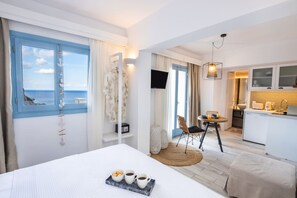 A hotel room with a bed, a dining area, a kitchen, and a view of the sea. - Yploui Suites 2 in Kira Panagia (Karpathos)