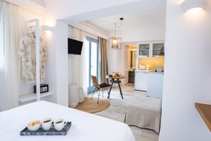 A hotel room with a bed, a small dining table with chairs, a kitchen area, and a TV mounted on the wall. - Yploui Suites 2 in Kira Panagia (Karpathos)