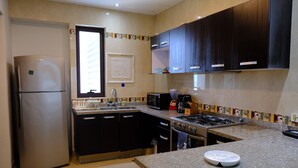 Une cuisine équipée d’un réfrigérateur, d’une cuisinière, d’un four à micro-ondes et de meubles de rangement de couleur sombre.