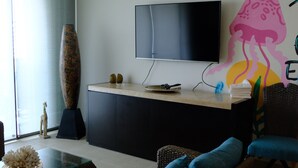Un salon moderne avec un canapé, une table basse en verre, un téléviseur fixé au mur et un grand vase.