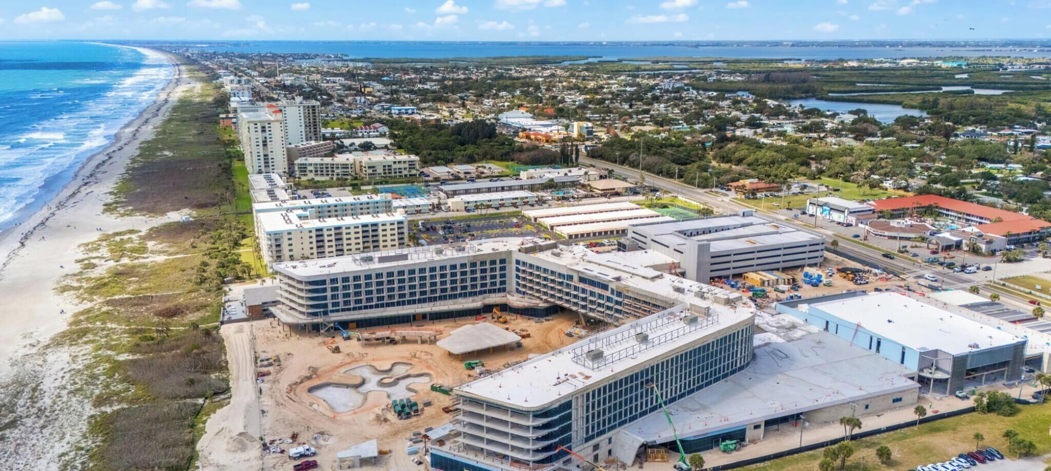 A coastal area with a beachfront hotel, a large commercial building under construction, and a marina.
