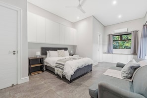 A bedroom with a bed, bedside table, and a window with curtains. - Bay House - Staynest Guesthouse (Ballito)