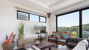 A modern living room with a sofa, a coffee table, a TV, and a balcony with a view. - Bay House - Staynest Guesthouse (Ballito)
