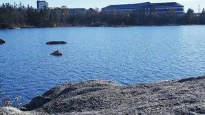Un lago con una orilla rocosa y edificios al fondo.