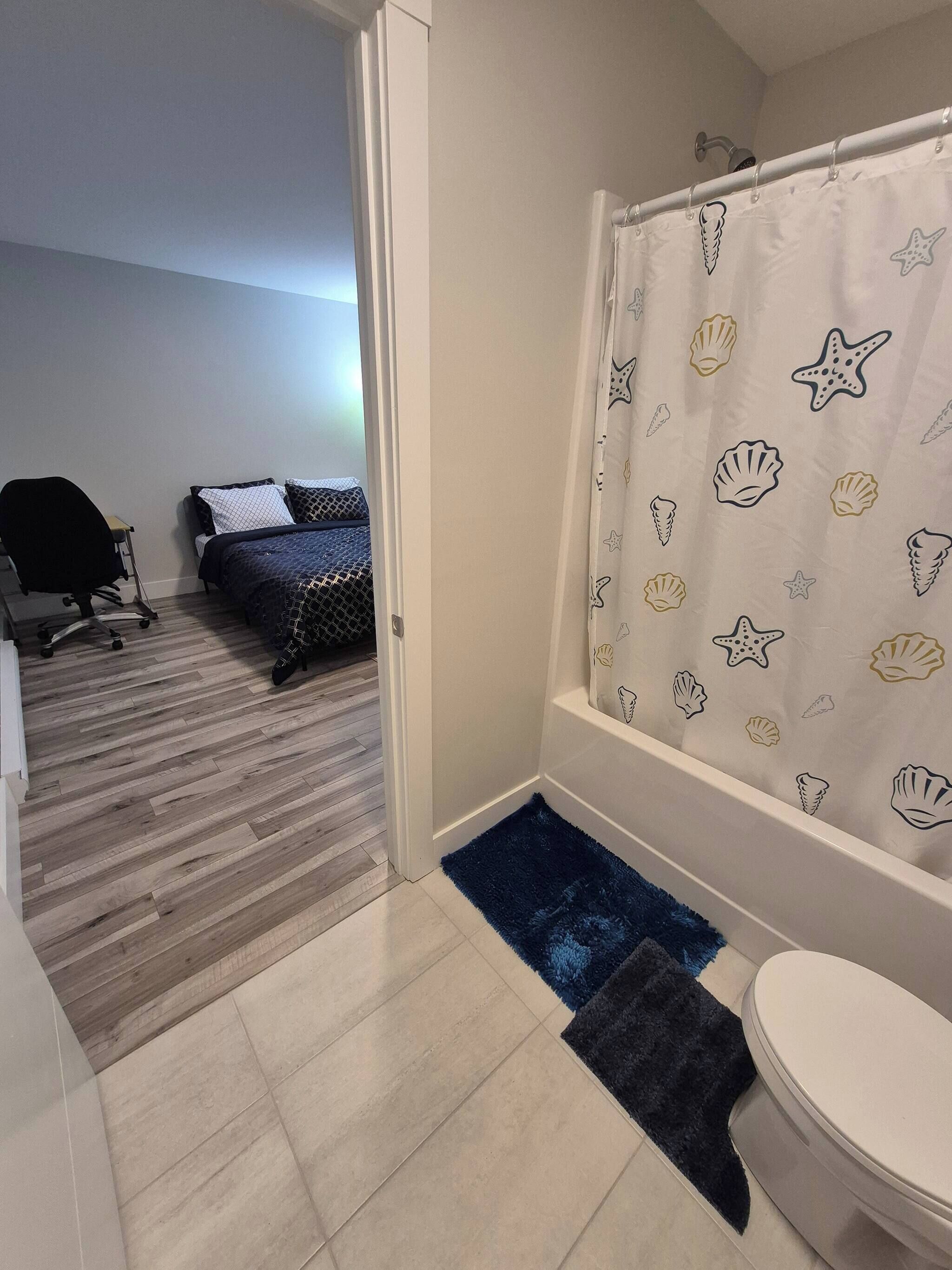A bathroom with a shower curtain featuring sea shell and starfish patterns, a toilet, and a small rug.