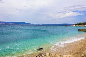 Ein Küstenstrand mit klarem türkisblauem Wasser, einer felsigen Küstenlinie und in der Ferne Hügel.