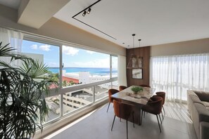 Ein modernes Wohnzimmer mit großem Fenster, einem Essbereich mit Tisch und Stühlen sowie einer Couch.