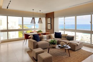Ein modernes Wohnzimmer mit großem Fenster, einer Sofagarnitur, einem Couchtisch und einem Essbereich.