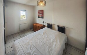 A bedroom with a bed, a wooden nightstand, a window, a radiator, and a wall-mounted light fixture. - Gorgeous apartment in Narbonne with house sea view (Narbonne)