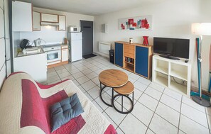 En kompakt opholdsstue med tekøkken, en sofa med puder, et fjernsyn og et lille bord.