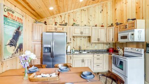 A wooden cabin interior with a kitchen, dining table, and a poster on the wall. - Island Gem, Private Yard, Fire Pit, Patio Dining, Pellet Smoker and Gas Grills (Kelleys Island)