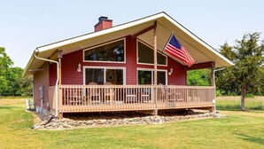 A red building with a porch, a flag, and a stone foundation. - Island Gem, Private Yard, Fire Pit, Patio Dining, Pellet Smoker and Gas Grills (Kelleys Island)