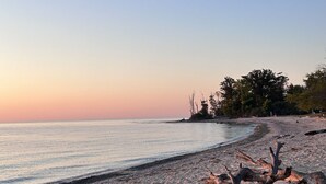 A beach with a fallen tree trunk, pebbles, and a clear sky. - Island Gem, Private Yard, Fire Pit, Patio Dining, Pellet Smoker and Gas Grills (Kelleys Island)