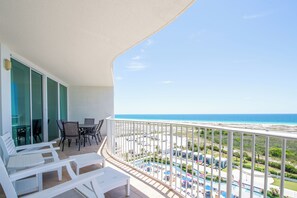 Ein Balkon mit weißer Möbel, ein Poolbereich und Blick auf den Strand.
