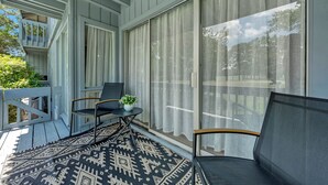 A covered porch with a black chair, a small table with a plant, and a patterned rug.