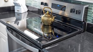 A modern kitchen with a stainless steel oven, a digital clock, and a gold teapot on the stove.