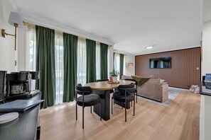 Una sala de estar moderna con una mesa redonda, cuatro sillas, un sofá, un televisor montado en la pared y una cafetera.