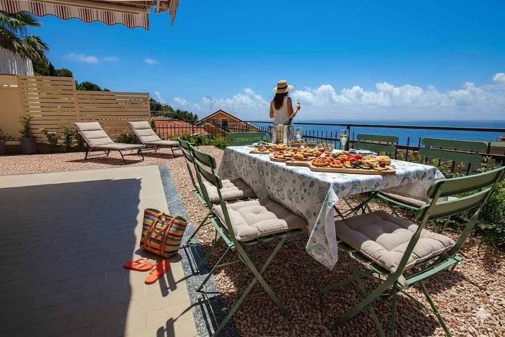 A terrace with a table set for a meal, outdoor seating, and a view of the sea.