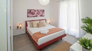 A bedroom with a bed, bedside lamps, a wall art piece, and a potted plant. - Holiday apartment with air conditioning and balcony (Piani Paorelli)