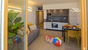 A modern living room with a sofa, a dining table with yellow chairs, and a kitchen area with a microwave and oven. - Holiday apartment with air conditioning and balcony (Piani Paorelli)