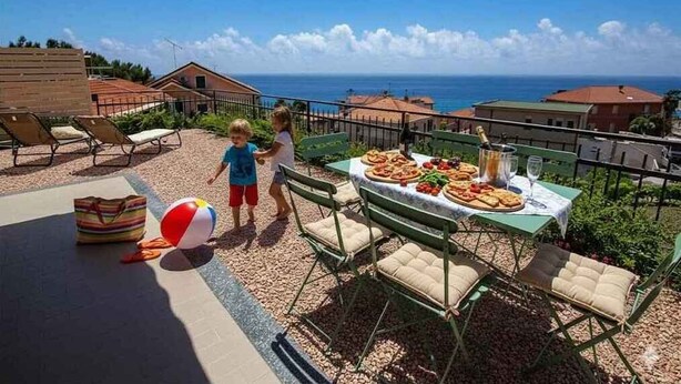 An outdoor dining area with a table set for a meal, overlooking a coastal view. - Holiday apartment with air conditioning and balcony (Piani Paorelli)