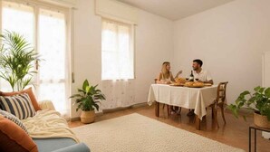 Un salón con un sofá, una mesa de comedor con dos personas y una planta en maceta.