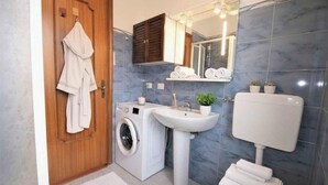 Un baño con puerta de madera, lavadora, lavabo, inodoro y espejo.