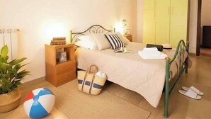 Un dormitorio con cama, mesita de noche, lámpara, armario y una planta.
