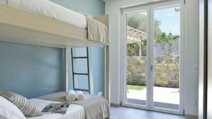 Ein Schlafzimmer mit Etagenbett, einem kleinen Tisch, einem Stuhl, einem Koffer, einem Hut und einer Schiebetür zu einem Außenbereich.