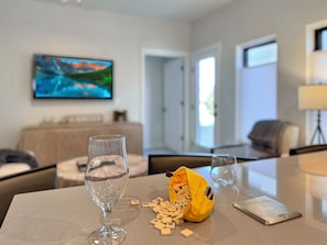 A living room with a television, a sofa, a coffee table with a wine glass, a bag of letter tiles, and a game board. - Basecamp - Ski·Golf·Fish·Lake - Fire Table + Views (Granby)