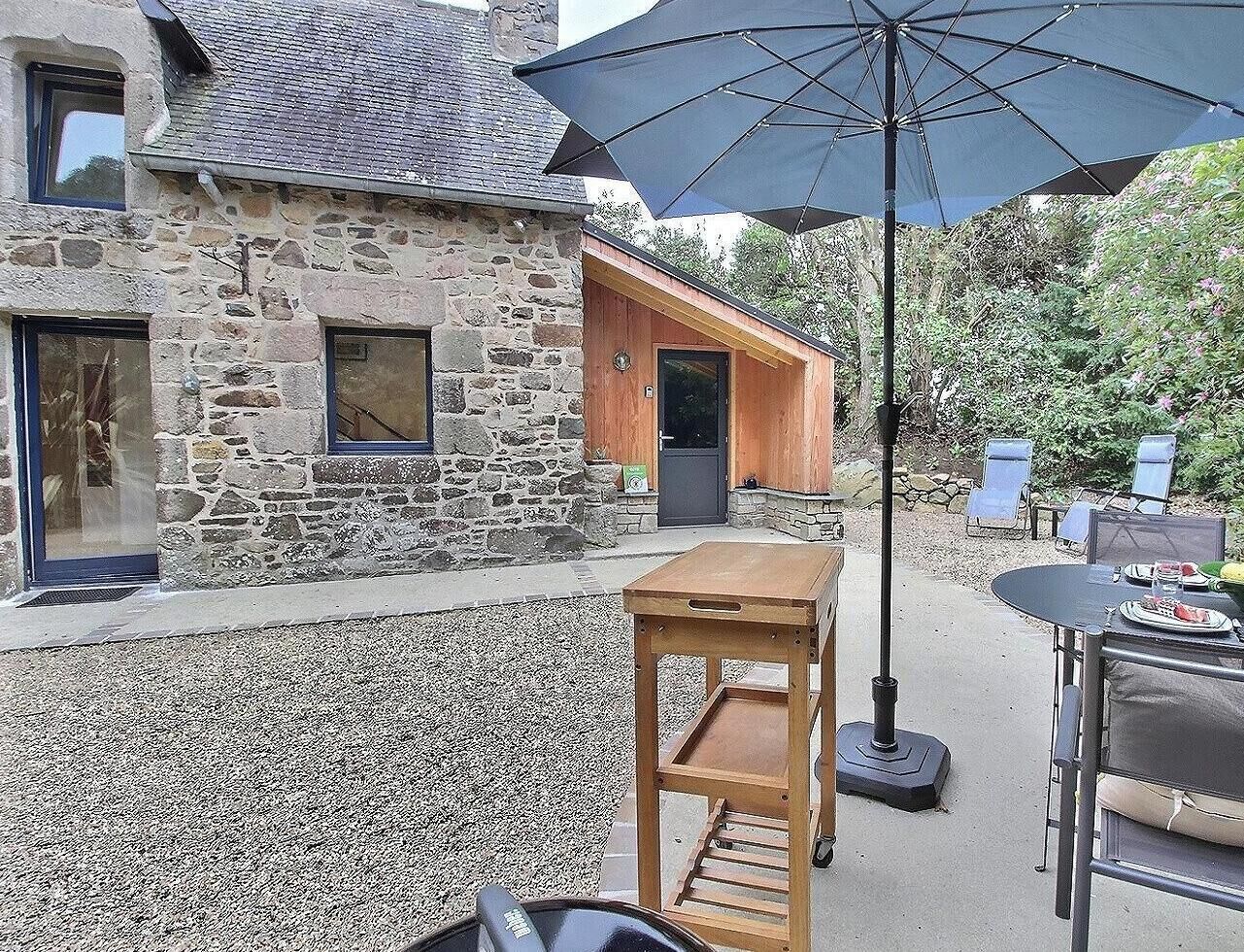 Un bâtiment en pierre avec une porte en bois, une table avec des chaises et un parapluie.