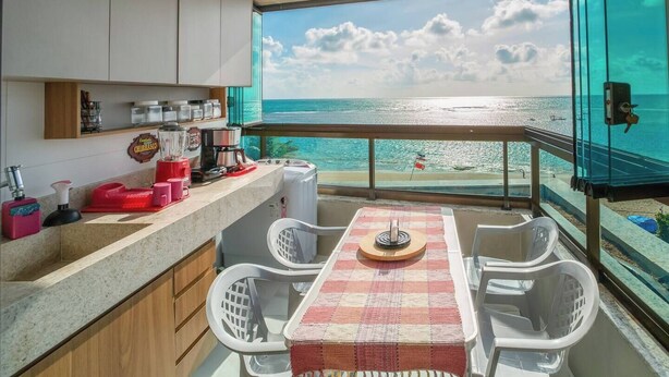 Ein Balkon mit Blick auf den Strand, ein Tisch mit Stühlen und eine Küchenzeile mit Geräten und Geschirr.