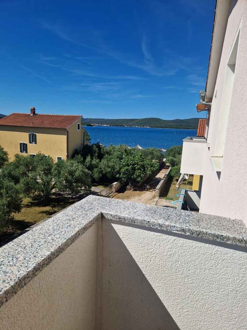 A balcony with a view of a coastal landscape, including a building with a red roof and a body of water in the distance.