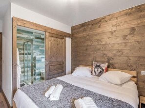 Ein Schlafzimmer mit einem hölzernen Kopfende, einem Bett mit weißer Bettwäsche, einer Glastür zu einem Badezimmer und einem Kissen mit Wolfsmotiv.