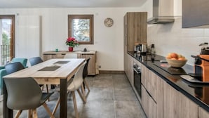 Una cocina moderna con zona de comedor, armarios de madera, encimera negra e iluminación colgante.
