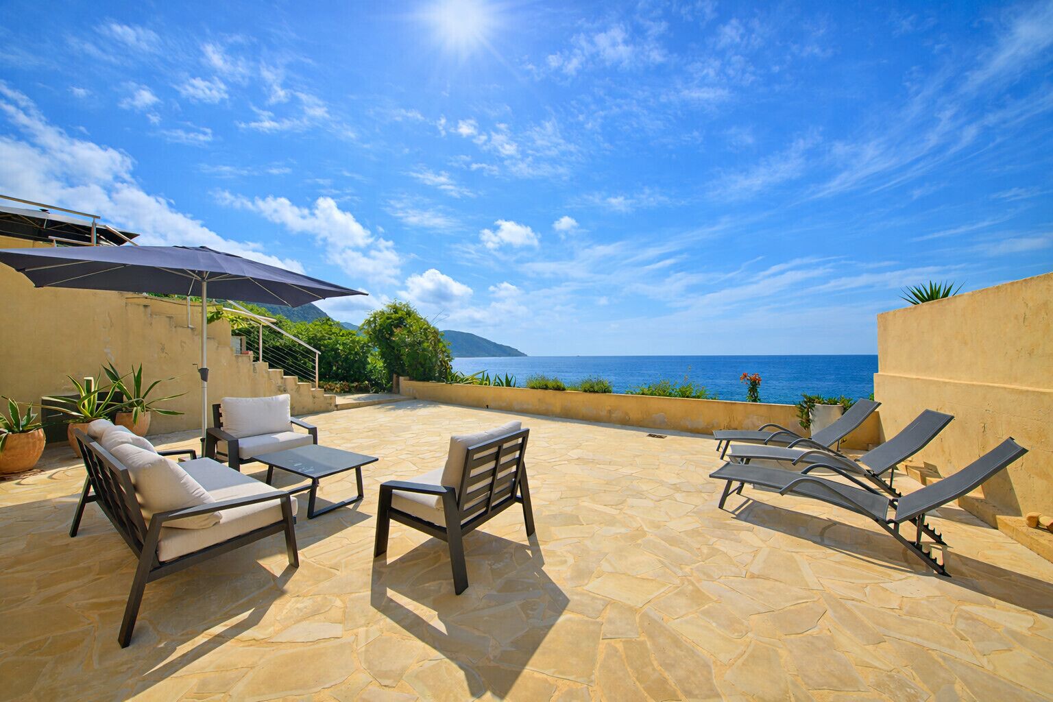 An outdoor patio with lounge chairs, a table, and potted plants.