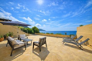 An outdoor patio with lounge chairs, a table, and potted plants. - Villa Stretta d’A Pianedda – 180° Ocean View - Welkeys (Villanova)