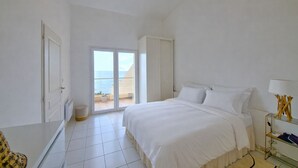 Une chambre avec un grand lit, une porte et une porte-fenêtre coulissante donnant sur un balcon, ainsi qu’une petite table avec une lampe.