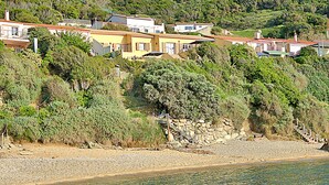 Un quartier résidentiel situé sur la côte, avec des maisons construites sur une colline, une plage rocheuse et une vue dégagée sur la mer.