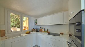 Une cuisine moderne avec des meubles blancs, un four encastré et une fenêtre donnant sur un espace verdoyant.